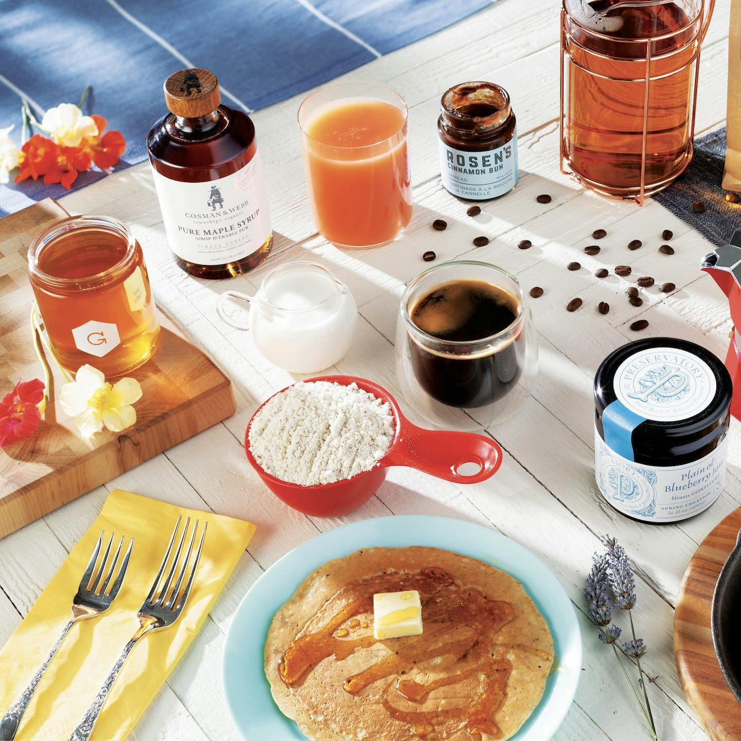 A breakfast table with pancakes, coffee, tea, maple syrup, honey and jam